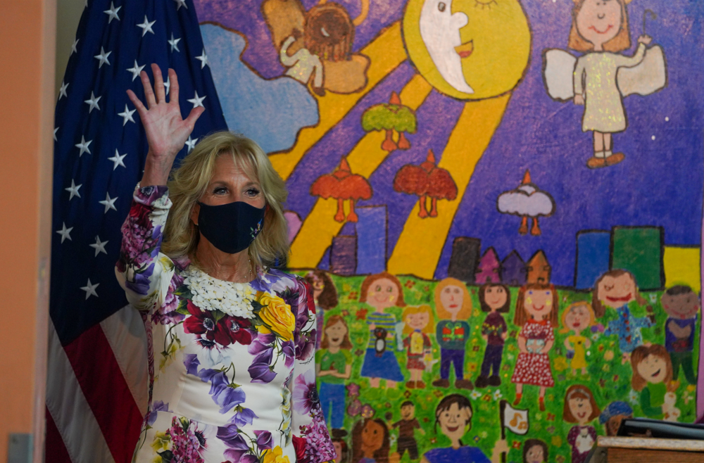 First Lady Jill Biden stands in front of a colorful mural at ceremony and waves